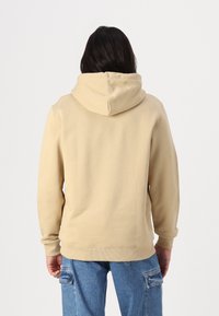 Beige hoodie made of soft fabric, featuring a large hood, ribbed cuffs, and a slightly textured surface. Casual design with no patterns.