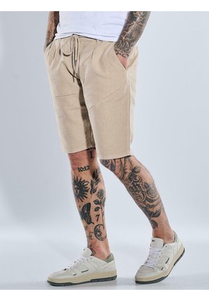 Beige shorts made of lightweight fabric with a drawstring waist, side pockets, and a straight cut. Worn with white and green sneakers.