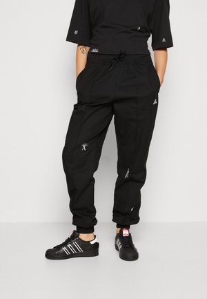 Zwarte cargobroek met trekkoord in de taille, geborduurde accenten in het wit en taps toelopende benen; gedragen met zwarte sneakers met witte strepen.