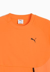 Lys orange Puma t-shirt med rund hals, sort Puma-logo på brystet og synligt nakke-label med størrelse medium.