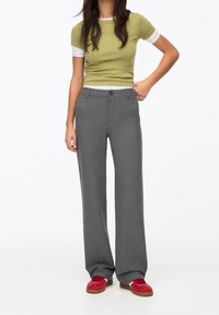 Grijze tailored broek met een rechte pijpstijl, gecombineerd met een aangesloten olijfgroene top met korte mouwen en een lichtgrijze onderlaag.