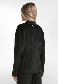 Top in corduroy nero con una finitura testurizzata, maniche lunghe e un discreto dettaglio con spacco sul retro. Il tessuto presenta strisce verticali strette.