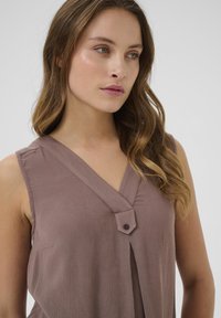 Mouwloze top met V-hals in een mauve gestructureerde stof. Kenmerkt zich door een knoopdetail en een geplooid ontwerp, wat leidt tot een elegante drape.