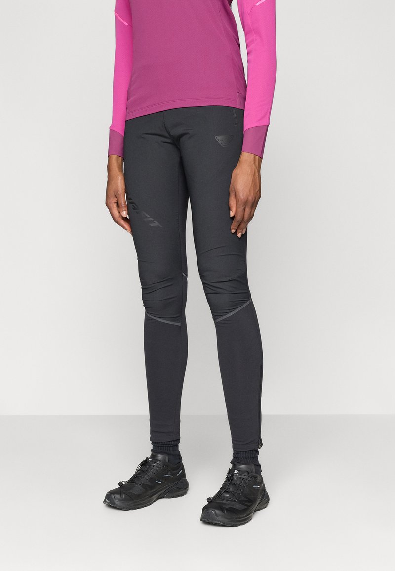Zwarte aansluitende hardloopleggings met textuuraccenten, gecombineerd met een lange mouw roze top en zwarte sportschoenen met veters.