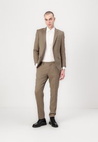 Completo marrone a scacchi con vestibilità su misura, abbinato a una camicia bianca. Scarpe stringate nere completano il look. Tessuto morbido e design elegante.