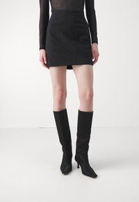 Czarna mini spódnica o dopasowanym kroju i widocznymi detalami szwów, zestawiona z czarnymi, wysokimi do kolan, skórzanymi botkami na obcasie o elastycznej teksturze.