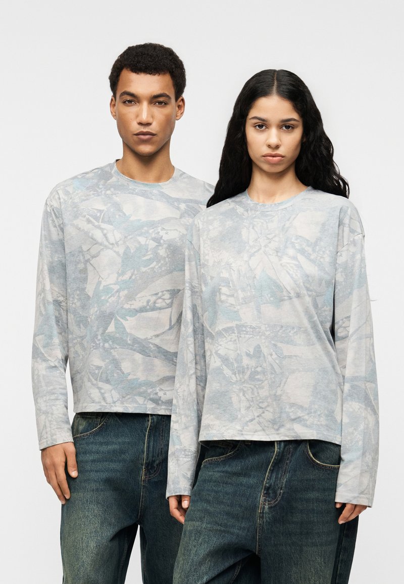 Ανοιχτό γκρι μακρυμάνικα πουκάμισα με αφηρημένα μπλε σχέδια, με χαλαρή εφαρμογή και λαιμόκοψη crew, συνδυασμένα με σκούρα τζιν.