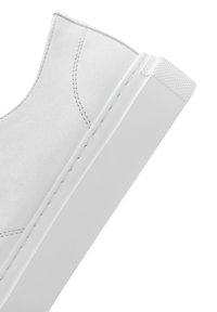 Baskets blanches en cuir à enfiler avec une semelle en caoutchouc texturée, présentant des lignes épurées et des coutures subtiles le long des côtés.