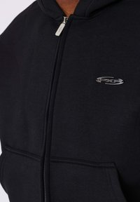 Sudadera con capucha negra con cremallera, hecha de mezcla de algodón. Cuenta con un bolsillo frontal y un logo plateado en el pecho. Textura suave con un ajuste estándar.
