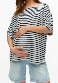 Randig oversized topp i grått och marinblått, kombinerad med ljusblå denimshorts. Toppen har vida ärmar, och modellen håller varsamt om en gravid mage.