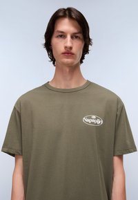 Olive green cotton t-shirt with a crew neck, short sleeves, and a white oval logo featuring "Napapijri" on the left side.