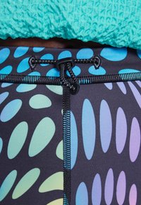 Pantaloni da nuoto neri con motivi a goccia multicolore in blu e lavanda. Presentano una coulisse nera e cuciture a contrasto.
