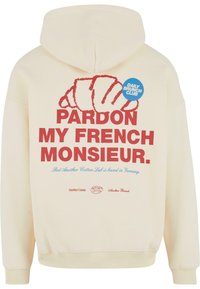 Kremowy hoodie z dużą czerwoną grafiką rogalika i tekstem "PARDON MY FRENCH MONSIEUR" w pogrubionej czcionce. Posiada niebieską okrągłą metkę z napisem "DAILY BRUNCH CLUB."