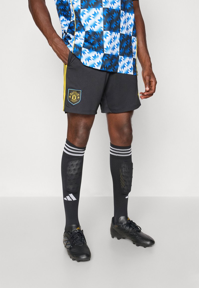 Sorte fodboldshorts med gule detaljer, mønstrede blå og sorte trøje, sorte sokker med hvide striber og sorte fodboldstøvler.