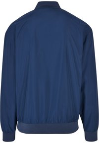 Námornícky modrá bomber bunda vyrobená z hladkej, ľahkej tkaniny. Má pletený golier a manžety, uvoľnený strih a elastický lem.