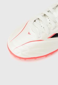 Άσπρο ποδοσφαιρικό παπούτσι μ ε κόκκινη σόλα και κόκκινα χαρακτηριστικά, με άσπρα κορδόνια και οπές κοντά στη γλώσσα, εμφανίζεται σε ανοιχτό φόντο.