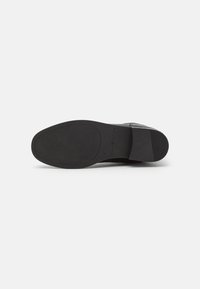 Semelle de chaussure en cuir noir avec une surface texturée, une forme arrondie et un détail de marque. Présente une finition lisse et un design de talon plat.