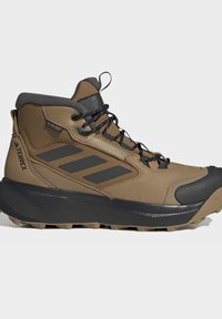 Brauner und schwarzer Adidas Terrex Mid-Top-Wanderschuh mit schwarzen Schnürsenkeln, robuster Sohle und Logostreifen an der Seite.