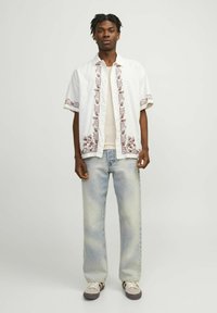 Hvid kortærmet skjorte med brune blomsterbroderier, beige undertrøje, lyseblå brede jeans og grå sneakers.