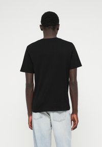 Μαύρη βαμβακερή μπλούζα με κοντά μανίκια και στρογγυλή λαιμόκοψη, φαίνεται από πίσω, σε συνδυασμό με ανοιχτόχρωμο τζιν παντελόνι.