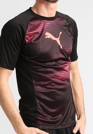 Mężczyzna noszący czarną i ciemnoczerwoną sportową koszulkę Puma z geometrycznym wzorem i dużym logo Puma na piersi.