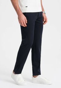 Marineblauwe slim-fit broeken van gladde stof, met een strak ontwerp, vlakke voorzijde en zijzakken, gecombineerd met witte sneakers.