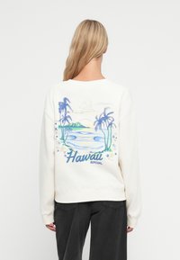 Kremowy sweatshirt z niebiesko-zieloną grafiką przedstawiającą plaż�ę z palmami oraz napisem "Hawaii". Wygodny, luźny krój.