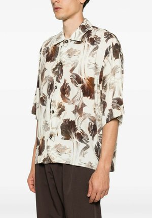 Uomo che indossa una camicia a maniche corte con bottoni con motivo astratto di piume marroni e beige, abbinata a pantaloni marrone scuro.