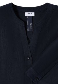 Chemise en lin bleu marine foncé avec col rond, boutonnée sur le devant et manches longues, avec étiquette de marque "CECIL" à l’intérieur du col.