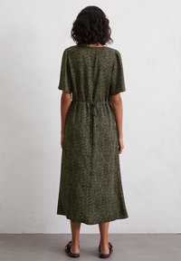 Green, patterned midi dress with short sleeves and a drawstring waist, featuring a flowing shape and soft texture. Worn with flat sandals.