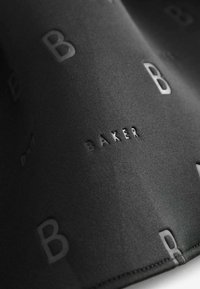 Tela negra con un acabado texturizado que presenta letras 'B' embosadas repetidas y la palabra 'BAKER' en un estilo contrastante.