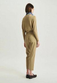 Pull en khaki et pantalon assorti, design ajusté, texture lisse, associé à des mocassins sombres et une écharpe bleu clair au cou.