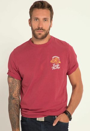 Camiseta de algodón roja con mangas cortas y puños enrollados. Presenta un estampado gráfico en el pecho que dice "Herencia del Águila Americana".