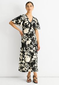 Schwarzes Blumen-Kleid mit V-Ausschnitt, Schmetterlingsärmeln und fließender Silhouette. Es zeichnet sich durch weiße Blumenmuster auf einem einfarbigen schwarzen Hintergrund aus.