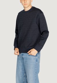 Felpa blu navy con stampa logo tonale, colletto a coste e maniche lunghe, abbinata a jeans azzurri.
