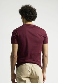 Camiseta de manga corta en color marrón, confeccionada en suave algodón, con un clásico cuello redondo y un diseño ajustado, combinada con chinos beige.