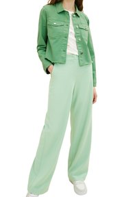 Giacca di jeans verde menta con tasche frontali, abbinata a pantaloni larghi verde menta. Sneakers bianche completano l'outfit, mostrando un look coordinato.