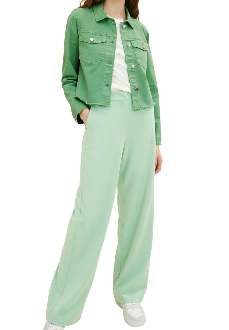 Giacca di jeans verde menta con tasche frontali, abbinata a pantaloni larghi verde menta. Sneakers bianche completano l'outfit, mostrando un look coordinato.
