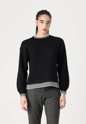 Pull en laine noir avec un col rond, présentant des accents rayés blancs au col et à l'ourlet. Manches longues avec une coupe décontractée.