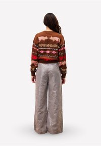 Bruine trui met meerkleurige patronen, gecombineerd met wijde, geblokte broek. Bevat een gestructureerde brei en contrasterende ontwerpelementen.