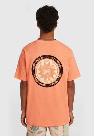 Lyhythihainen T-paita korallin värisenä, jossa takana pyöreä graafinen kuvio palmuineen ja tekstillä. Puuvillamateriaalia, rento istuvuus.