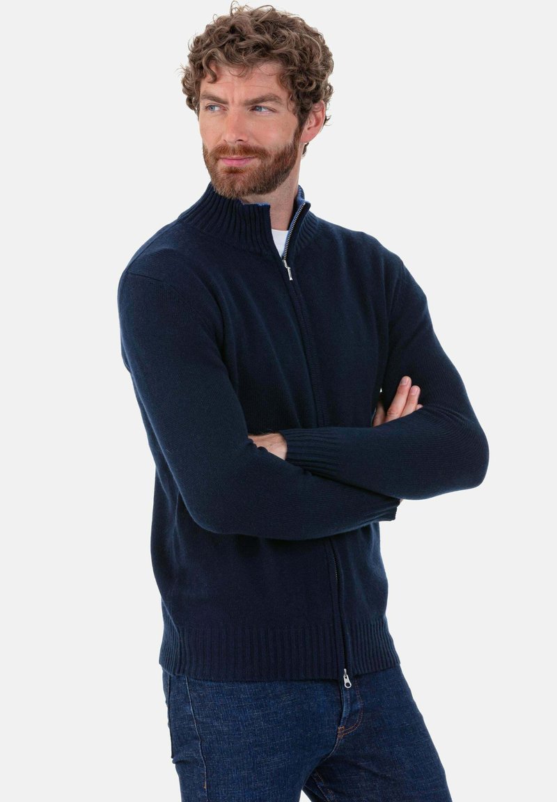 Pull zippé bleu marine avec col montant, poignets et ourlet côtelés. Fabriqué en tissu texturé, présentant une silhouette épurée et des détails de couture subtils.