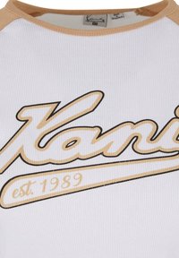 Hvit ribbestrikket T-skjorte med beige detaljer. Har "Kanji" i fet svart og gull skrifttype, med "est. 1989" under. Rund hals.