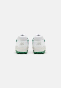 Vita sportskor med gröna accenter, med en texturerad ovandel, vadderad krage och gummisula. Logotyp synlig på hälen.