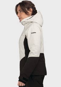 Damenjacke in Weiß und Schwarz, wasserdichtes Material, taillierte Passform, mit Reißverschlusstaschen, verstellbarer Kapuze und Logo auf dem Ärmel.