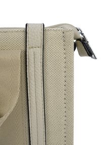 Close-up of beige textured fabric bag corner with stitched leather trim and silver zipper pull tab.