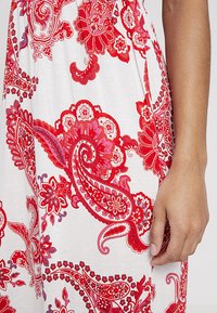 Rood en roze paisleypatroon op een witte jurk, gemaakt van lichte stof en met eenGathered taille en een zijsplit.