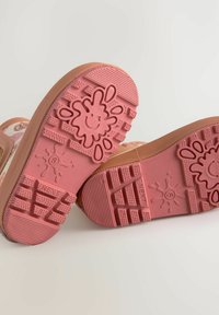 Zapatillas de goma rosas con suelas texturizadas que presentan un diseño de sol sonriente. Los acentos incluyen patrones multicolores en la parte superior del zapato.