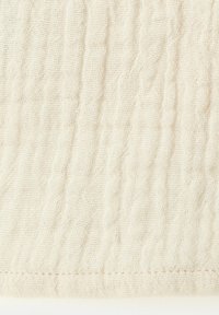 Tissu doux beige à tissage lâche avec de subtiles rides verticales, présentant une couture cousue au bord inférieur.