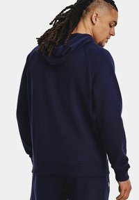 Felpa con cappuccio blu navy realizzata in tessuto morbido, con tasca a marsupio e polsini a costine, mostrata dal retro con dettagli di cucitura visibili.